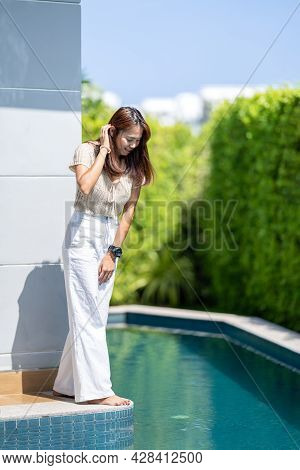 Asian Woman Is Looking Into Under The Pool Beside The Building With The Tree Background Environment.
