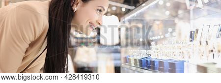 Smiling Young Woman Looks At Showcase With Jewelry