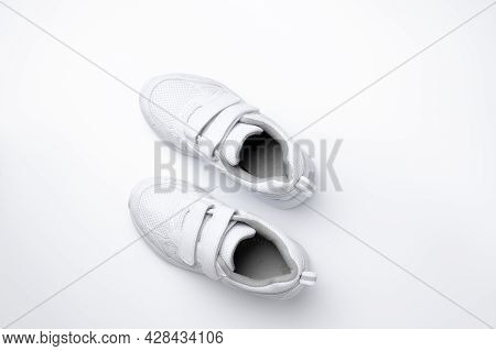 Minimalistic Flat Lay For Advertising Of White Kid Sports Shoes With Velcro Isolated On A White Back