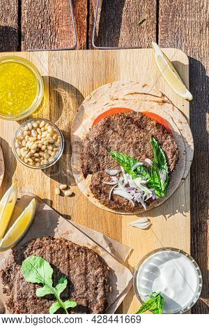 Lamb Kebab Patties Served With Mint Dip, Crunchy Salad, Pitta Bread And Raw Red Onions.