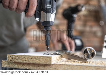 Screwing A Self-tapping Screw Into A Metal Fastening Hole On A Wood Strip Using A Screwdriver, The W