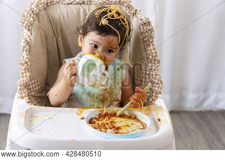 Adorable Little Funny Girl Eating Spaghetti With Spoon And Drinking Water From Bottle While Sitting 