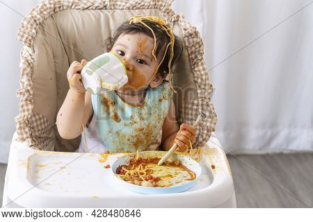 Adorable Little Funny Girl Eating Spaghetti With Spoon And Drinking Water From Bottle While Sitting 