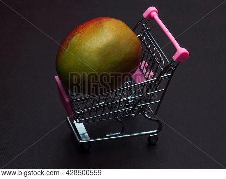 One Green Red Mango Is Lying In A Small Shopping Trolley. An Exotic Tropical Fruit In A Toy Metal Ca