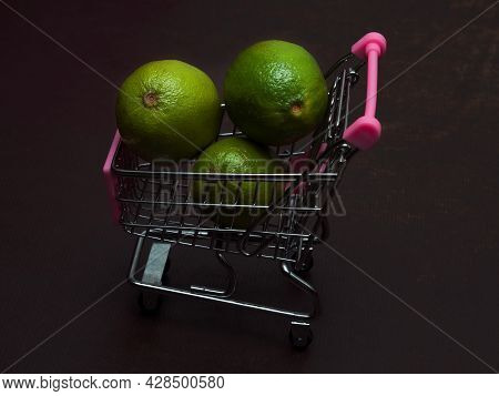 One Green Sour Lime Is In A Small Shopping Trolley. An Exotic Tropical Fruit In A Toy Metal Cart.