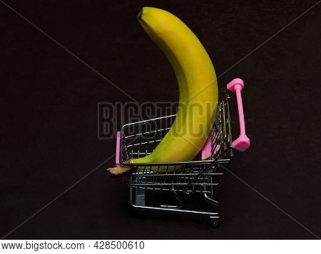 One Yellow Banana Is Lying In A Small Shopping Trolley. A Tropical Fruit In A Toy Metal Cart.