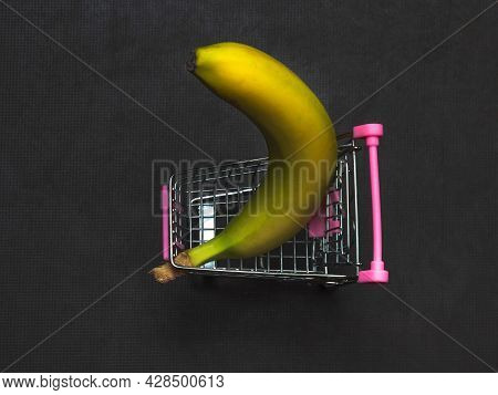 One Yellow Banana Is Lying In A Small Shopping Trolley. A Tropical Fruit In A Toy Metal Cart.