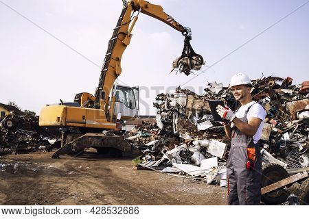 Man Controlling Process Of Industrial Scrap Metal Lifting At Junk Yard.