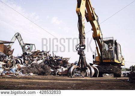Man Worker Operating Scrap Metal Recycling Machine In Junk Yard.