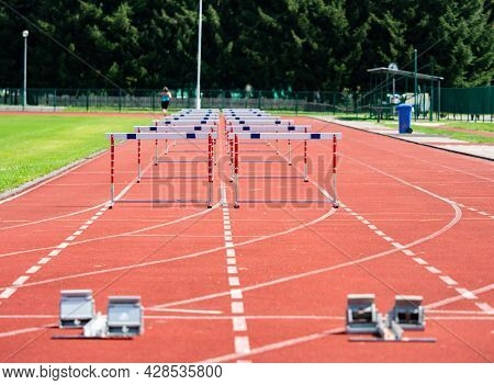 Hurdle On The Sprint Lane With Starting Blocks Against Blurry Background. Stadium With Two Hurdles T