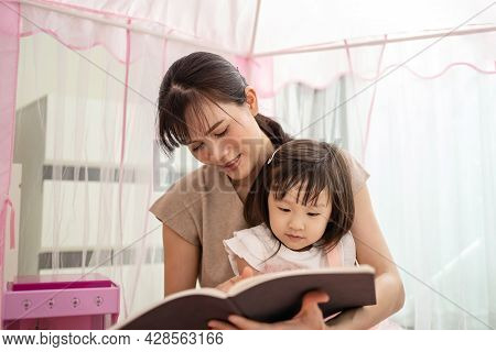 Asian Mom Read Storytale To Young Baby Girl Daughter In Tent At Home. Beautiful Mother Play Educatio