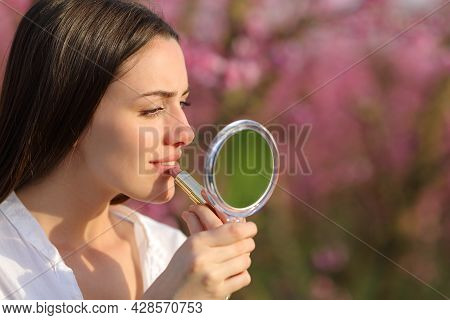 Beautiful Concentrated Woman Painting Lips Using Mirror In A Pink Field