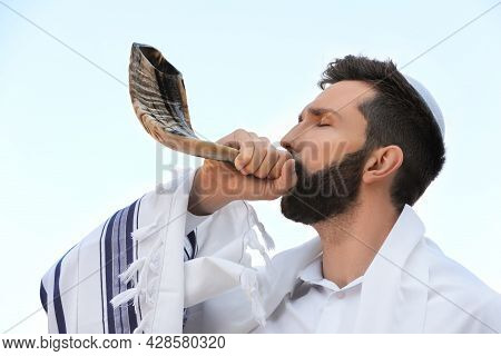 Jewish Man In Kippah And Tallit Blowing Shofar Outdoors. Rosh Hashanah Celebration