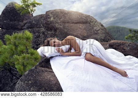 A Beautiful Young Girl Is Sleeping On The Rocks In The Mountains, A Snow-white Bed, Pillow And Sheet