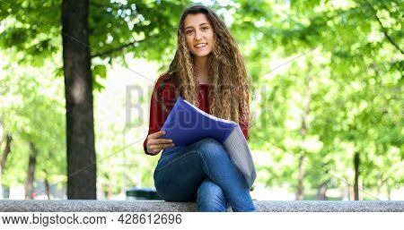 Beautiful female college student reading a book on a bench in a park