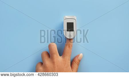 Medical Device For Hypoxia. Female Finger In A Pulse Oximeter On A Blue Background With Copyspace