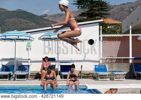 Ceriale, Italy - 13 July 2021: A Little Girl With A Frightened Expression Dives From The Trampoline 
