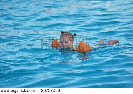 Happy Girl Swims In The Pool In Oversleeves And Wings. Child Safety In The Water. Cheerful Child Rej