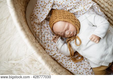 A Reborn Newborn Baby Doll Toy Dressed In A Mustard Colored Bonnet Hat And A White Cardigan Lying In