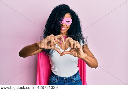 Middle age african american woman wearing super hero costume smiling in love doing heart symbol shape with hands. romantic concept. 