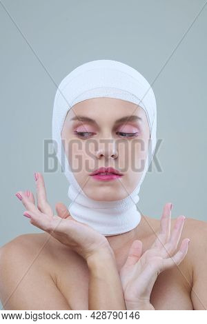 Graceful Young Woman In Head Bandage Having Makeup Gesturing Hands And Looking Down Against Isolated