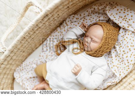 A Reborn Newborn Baby Doll Toy Dressed In A Mustard Colored Bonnet Hat And A White Cardigan Lying In