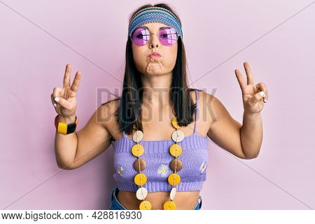 Young brunette woman wearing bohemian and hippie style doing peace symbol puffing cheeks with funny face. mouth inflated with air, catching air. 
