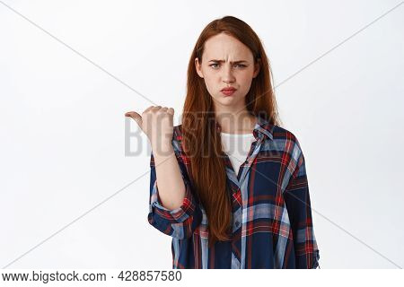 Flustered Young Redhead Girl Pointing Left And Frowning Upset, Stare Confused After Showing Advertis