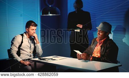 Medium Shot Of Detective Showing Picture Of Suspected Robbers Accomplice During Interview In Police 