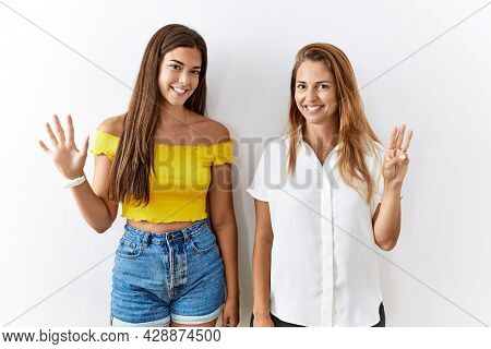 Mother and daughter together standing together over isolated background showing and pointing up with fingers number eight while smiling confident and happy. 