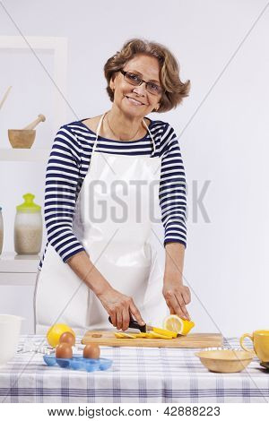 Vacker och glad äldre kvinna matlagning på hennes kök gör cookies