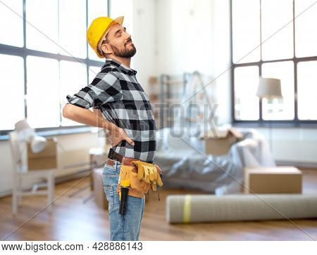 repair, construction and building concept - male worker or builder in helmet having back ache over home room background