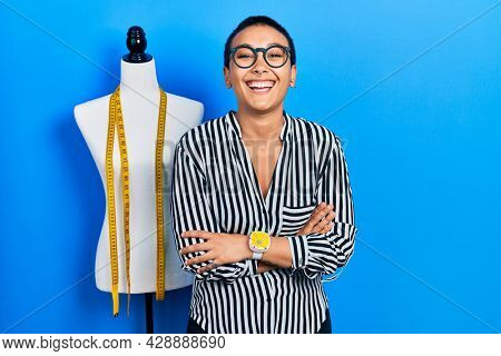 Beautiful hispanic woman with short hair standing by manikin with crossed arms smiling and laughing hard out loud because funny crazy joke. 