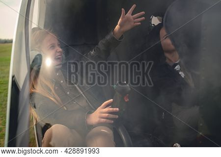 Happy Tween Girl In Aviator Headphones Sitting In Helicopter, Pointing To Sky