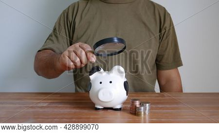 Asian Man Holding Magnifying Glass In Hand Looking Some Thing On Piggy Bank And Coins Stacking Ontab