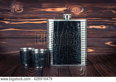 Hip Flask For Whiskey And Two Stainless Steel Lip Tumbler On A Dark Brown Wooden Table. Bar Tools. D
