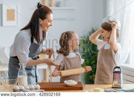 Happy loving family are preparing bakery together. Mother and children daughters girls are cooking cookies and having fun in the kitchen. Homemade food and little helper. 