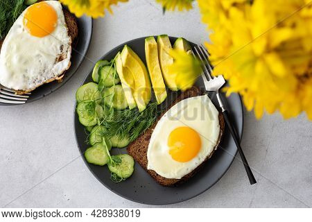 Delicious Breakfast With Avocado, Fresh Cucumbers And Microgreens Of Peas With Dill, Fried Eggs On B