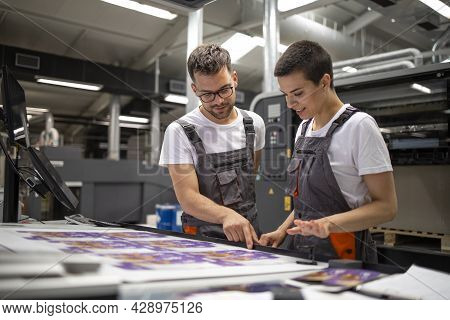 Printing Machine Operators Checking Graphic Quality And Color Values At Print House.