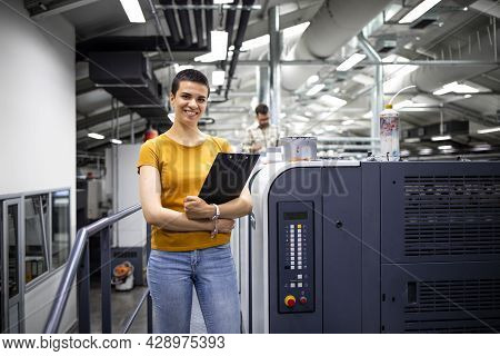 Portrait Of Talented Female Designer Standing By Modern Printing Machine In Print Shop.