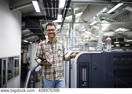 Portrait Of Print Manager Standing By Large Offset Printing Machine In Print Factory.