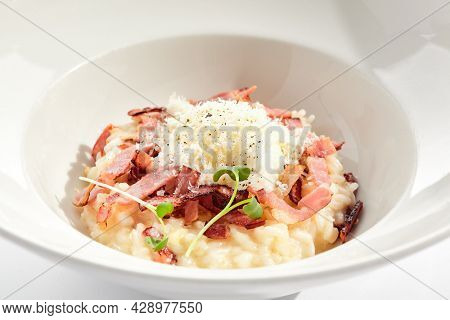 Risotto alla carbonara on white restaurant plate. Risotto with bacon and egg, garnished with micro greens. Risotto topped with parmesan cheese