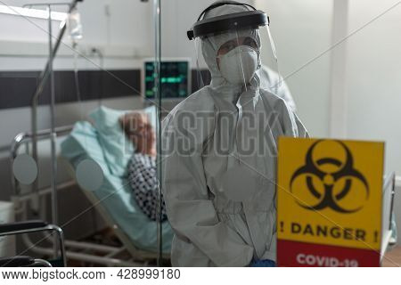Portrait Of Medical Nurse Dressed In Pee Suit In Hospital Room Looking At Camera, With Senior Woman 