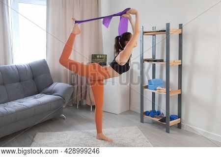 Young Woman In Sportswear Is Stretching Leg And Backbend With Resistance Band At Home. She Is Improv