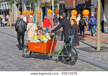Young Parents Carry Children In The Bicycle Stroller By Celebratory Street  In Dordrecht, Netherland