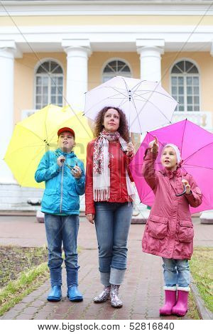 Mother with two children stand with colorful umbrellas, the girl points a finger upwards