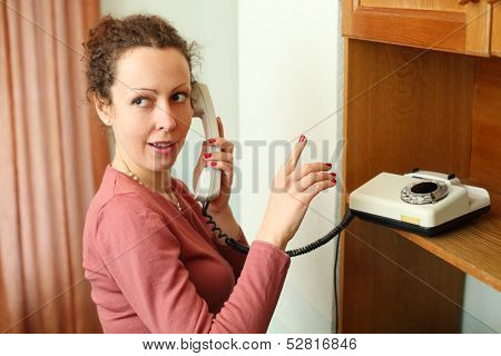 Young woman talking on a rotary phone and ask keep quiet finger gesture