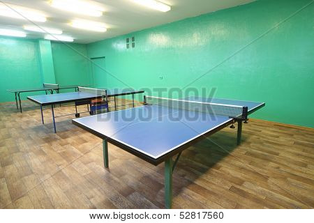 Three blue ping pong tables in the room with green walls