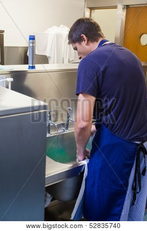 Kitchen porter standing behind sink in professional kitchen