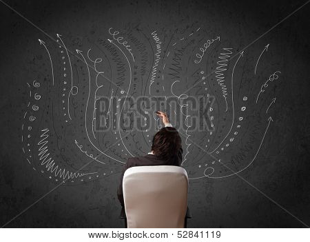 Thoughtful young businessman sitting and deciding in front of a chalkboard with sketched arrows and lines in different directions